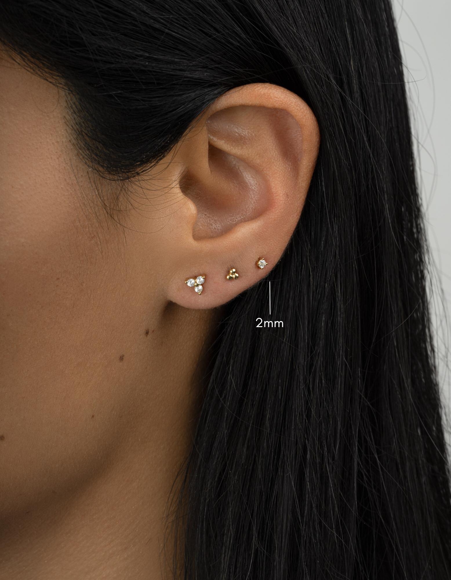 Closeup gold plated diamond solitaire stud earring layered on womens ear 