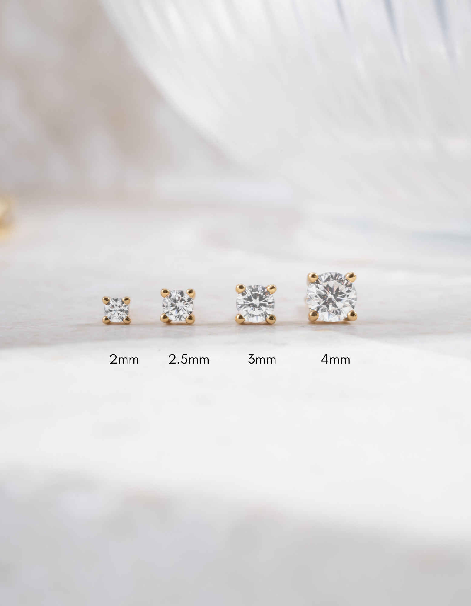 set of gold plated diamond solitaire stud earrings in varying sizes on white background