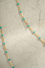 Close-up detail of gold turquoise enamel beaded necklace neutral background