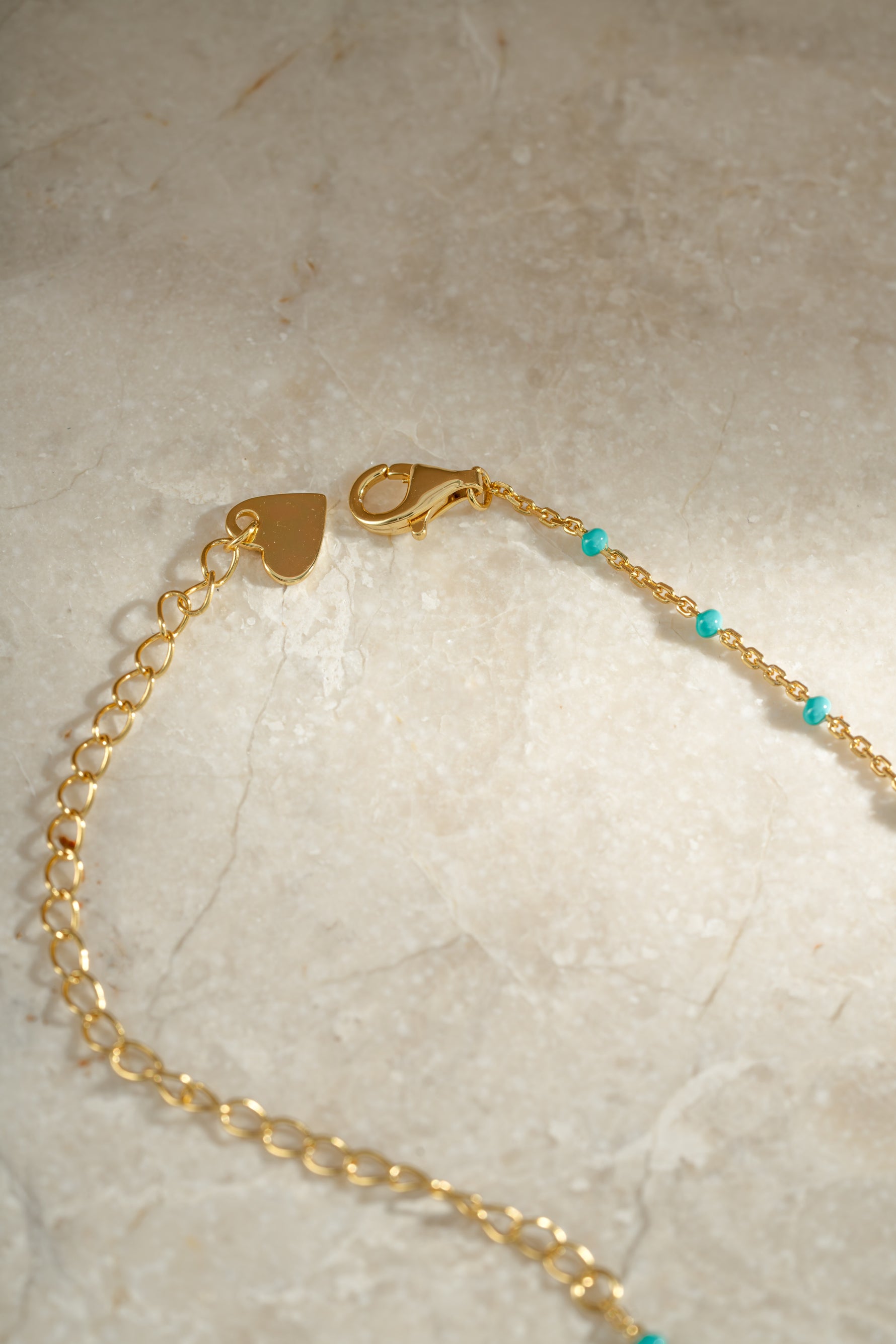 Close-up detail of clasp on gold turquoise enamel beaded necklace neutral background