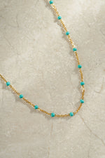 Gold turquoise enamel beaded necklace on neutral background