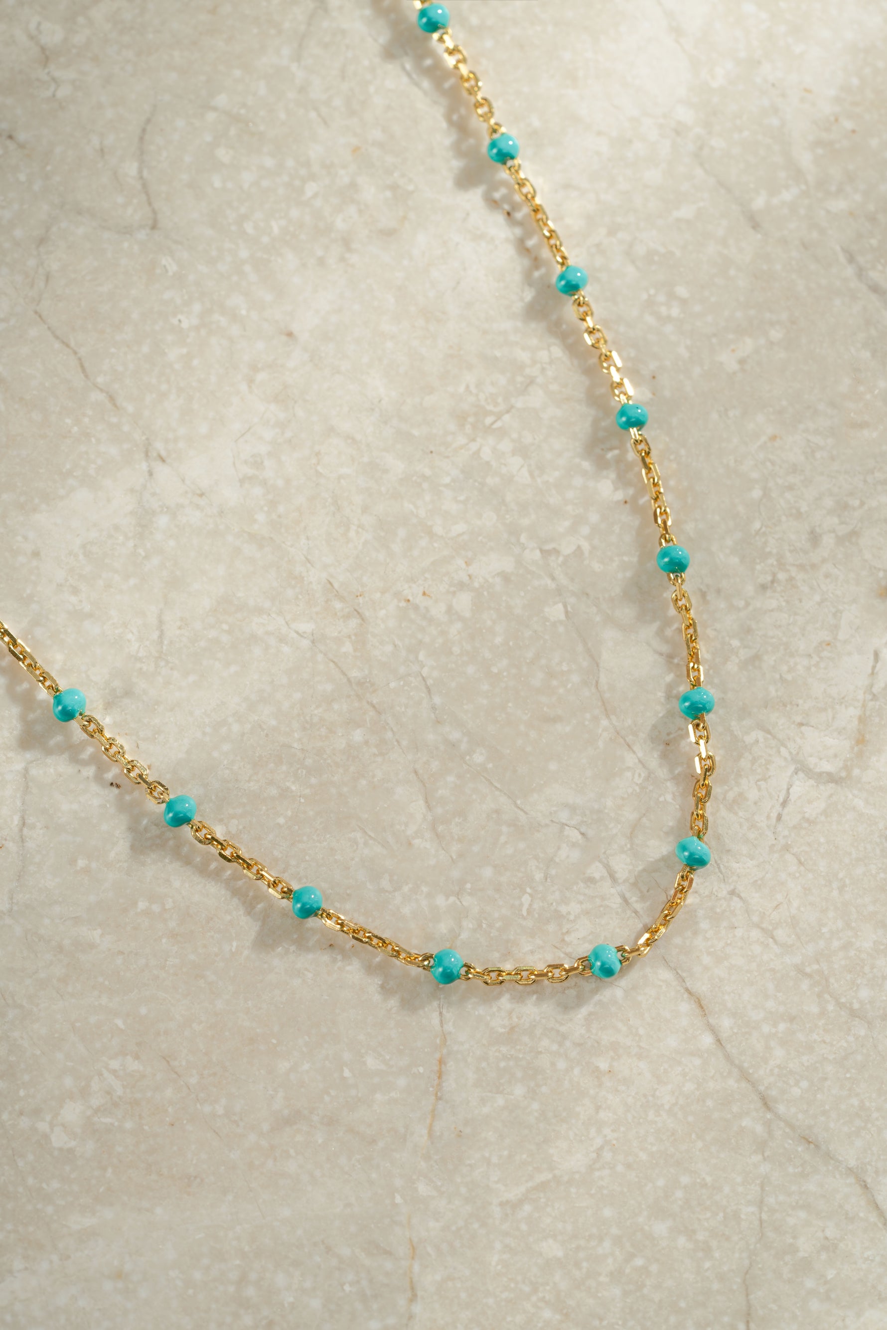 Gold turquoise enamel beaded necklace on neutral background