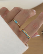 gold turquoise eternity ring with gold rings stacked on womens hand 