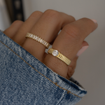 model wearing gold stacking rings, an eternity ring on the middle finger and a solitaire ring on the index finger. 