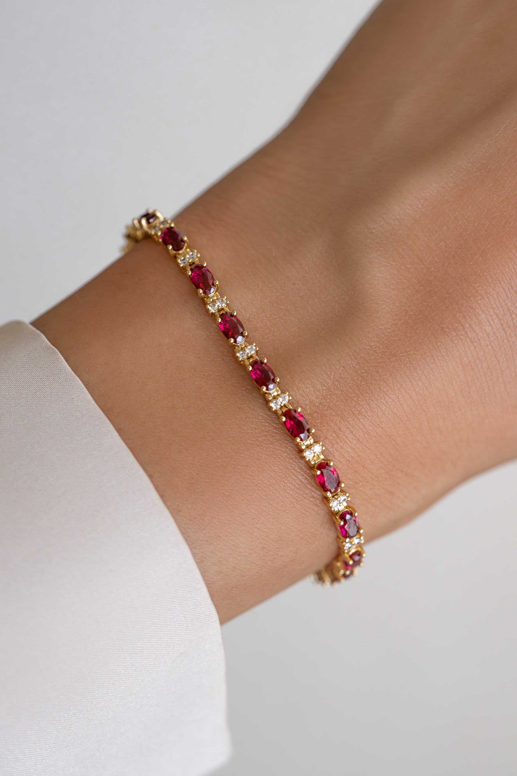 Gold Ruby Tennis Bracelet by Sami Jewels worn on wrist, featuring a row of vibrant ruby gemstones set in a gold bracelet.