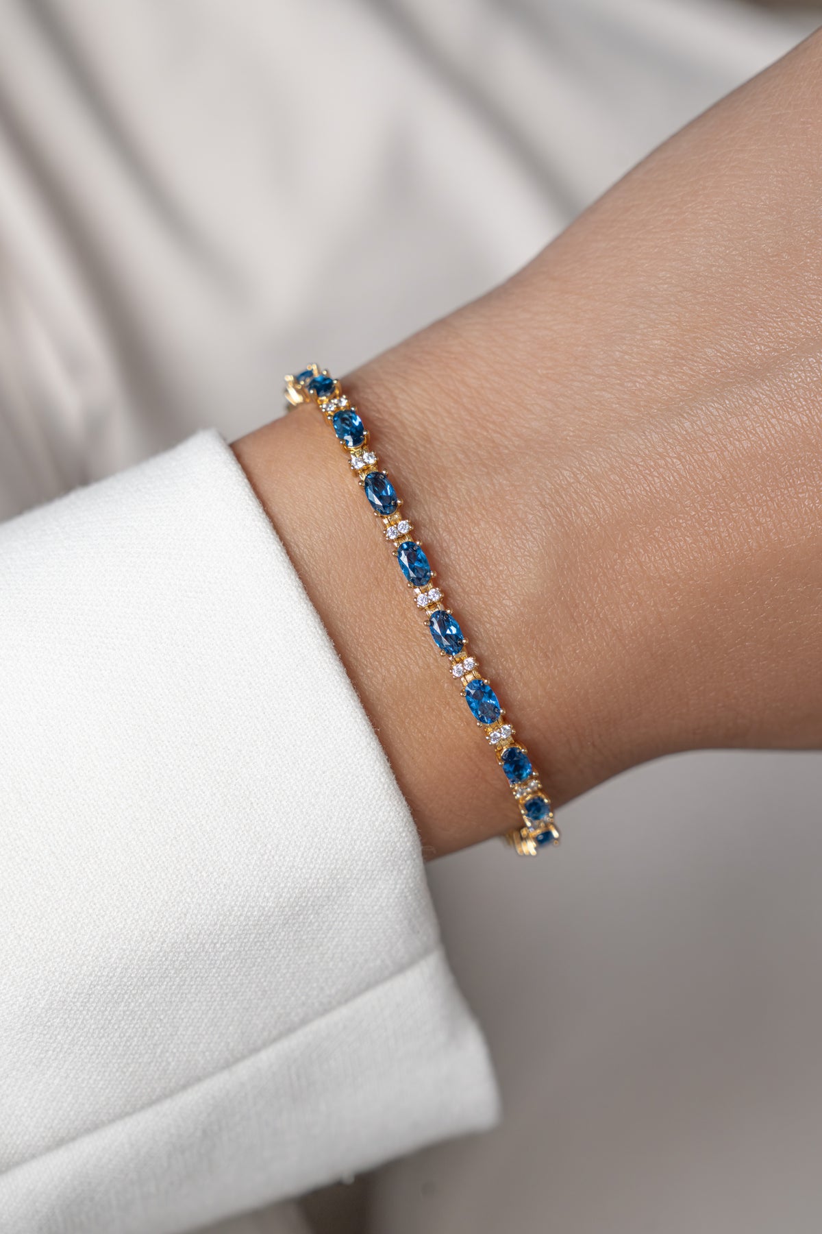An oval-cut sapphire bracelet with alternating white gemstones featured on a wrist. 