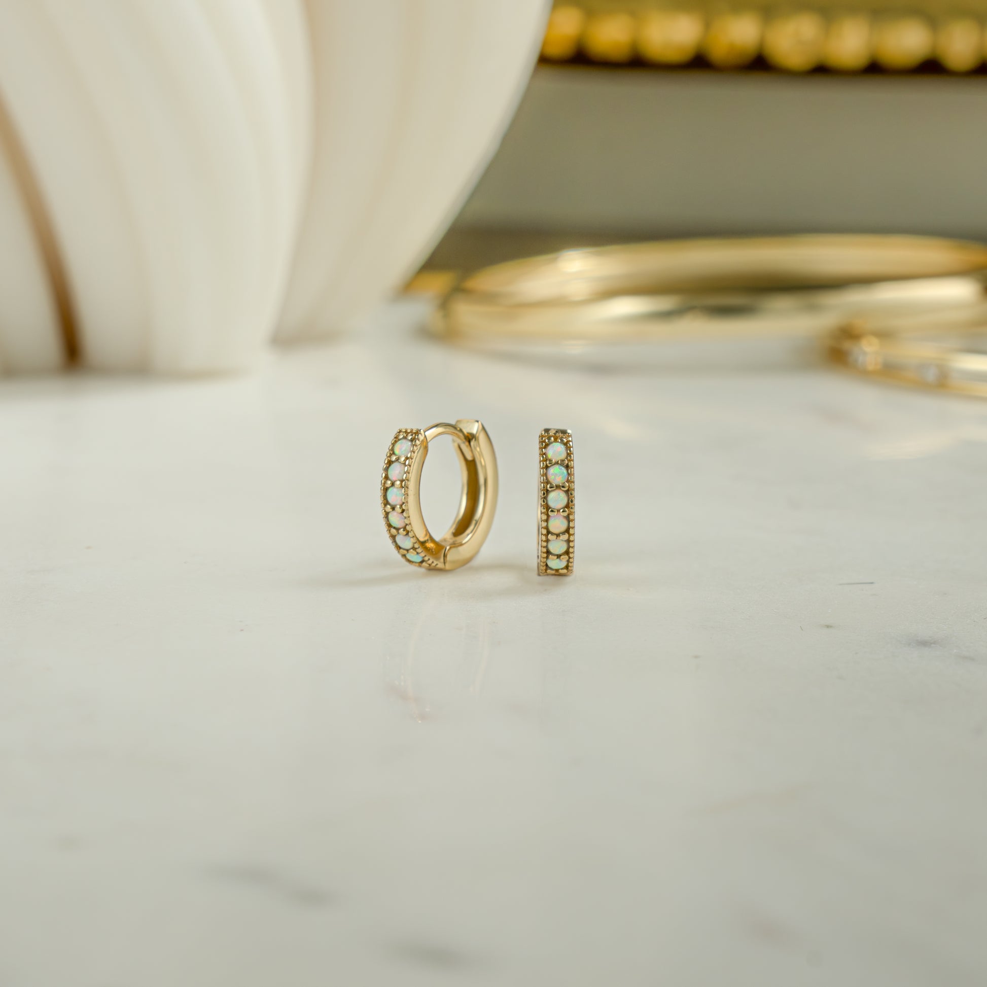 Close up image of dainty gold hoop earrings The aesthetic earrings feature  opal jewelry stones.