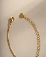 Close-up of the gold necklace's lobster clasp, extension chain and heart-shaped end tag.