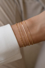 Gold box chain and satellite bracelets stacked with a paperclip-and-chain bracelet set.