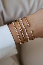 A styled model wearing a variety of stacked gold diamond bracelets, bangle, and cuff. 