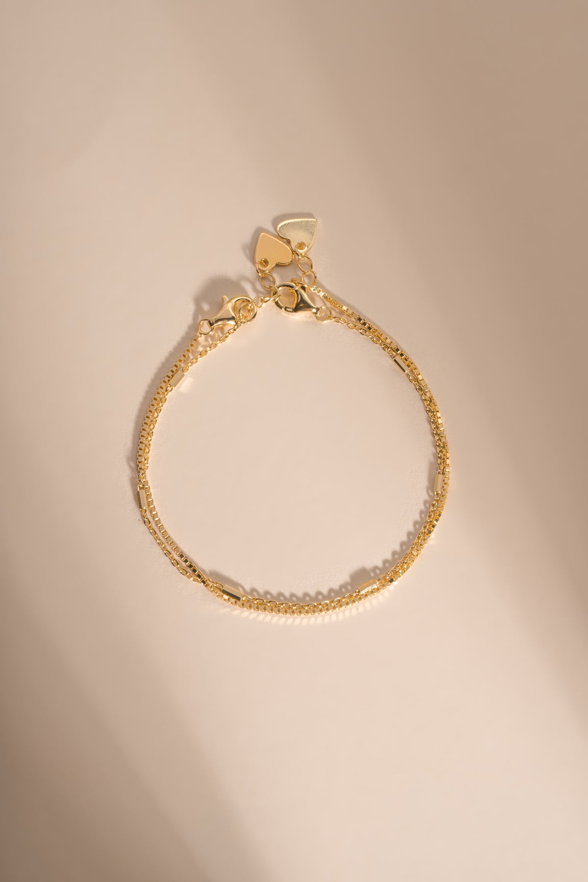 Gold box chain and satellite bracelets arranged together on a cream background.