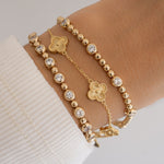 Model wearing a stack of gold diamond bracelets and four leaf clover bracelet in gold in the middle.