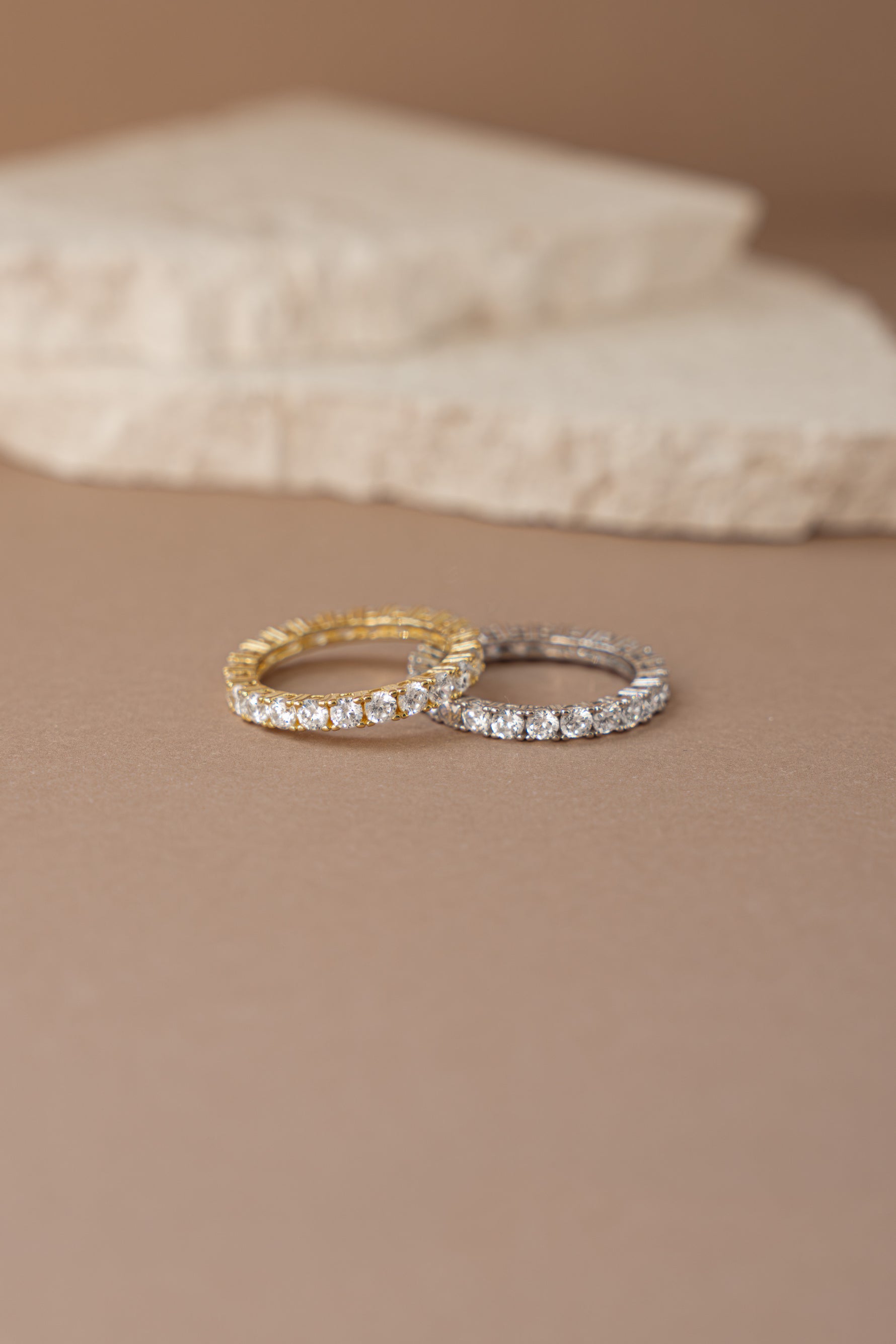 gold studded eternity ring and sterling silver studded eternity ring neutral background