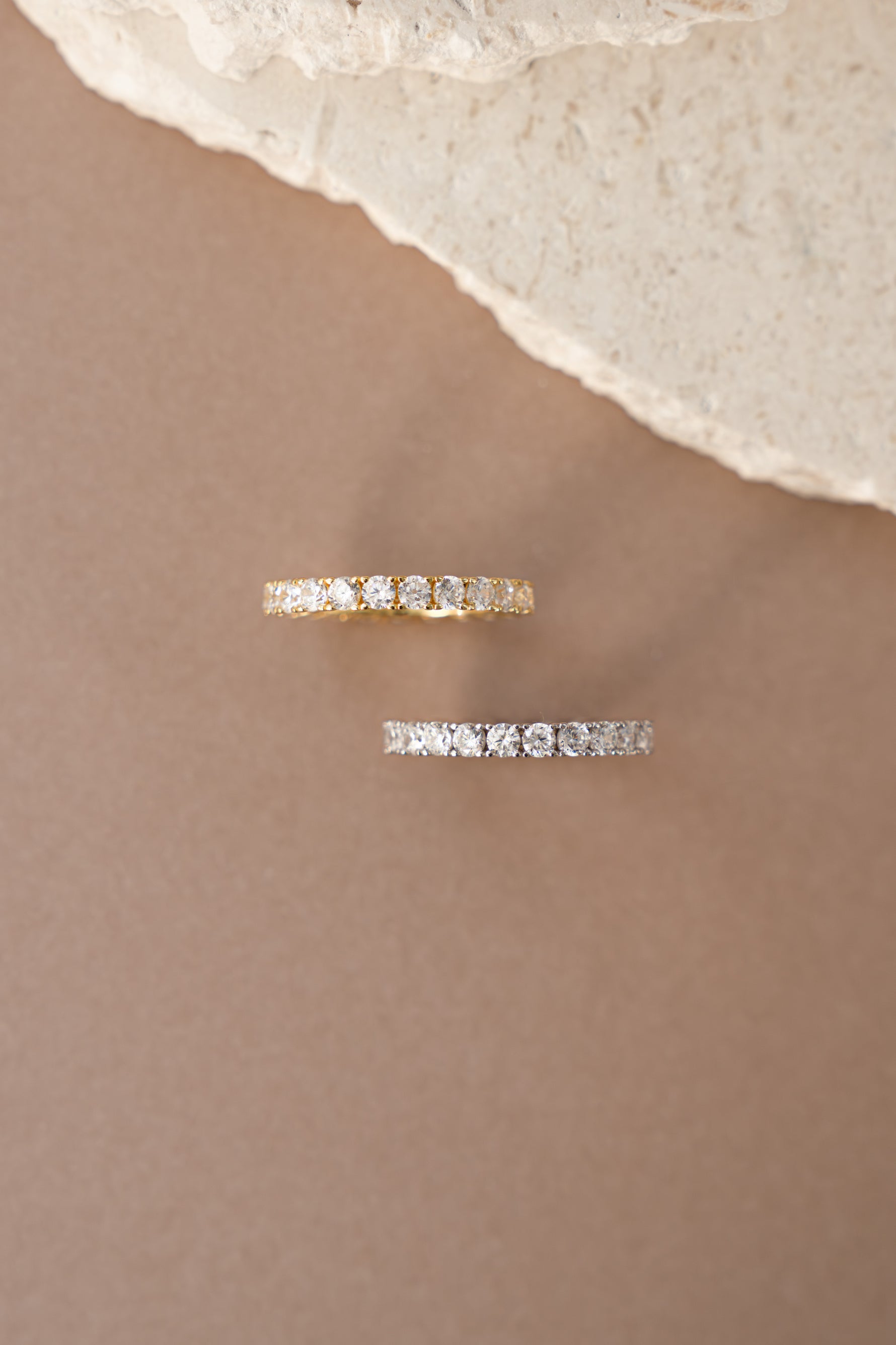 gold studded eternity ring and sterling silver studded eternity ring top view neutral background