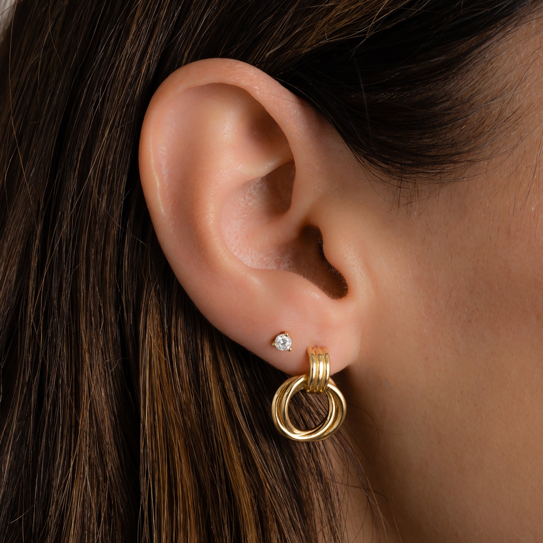 model wearing gold knot hoops mixed with dainty studs for a chic contrast.