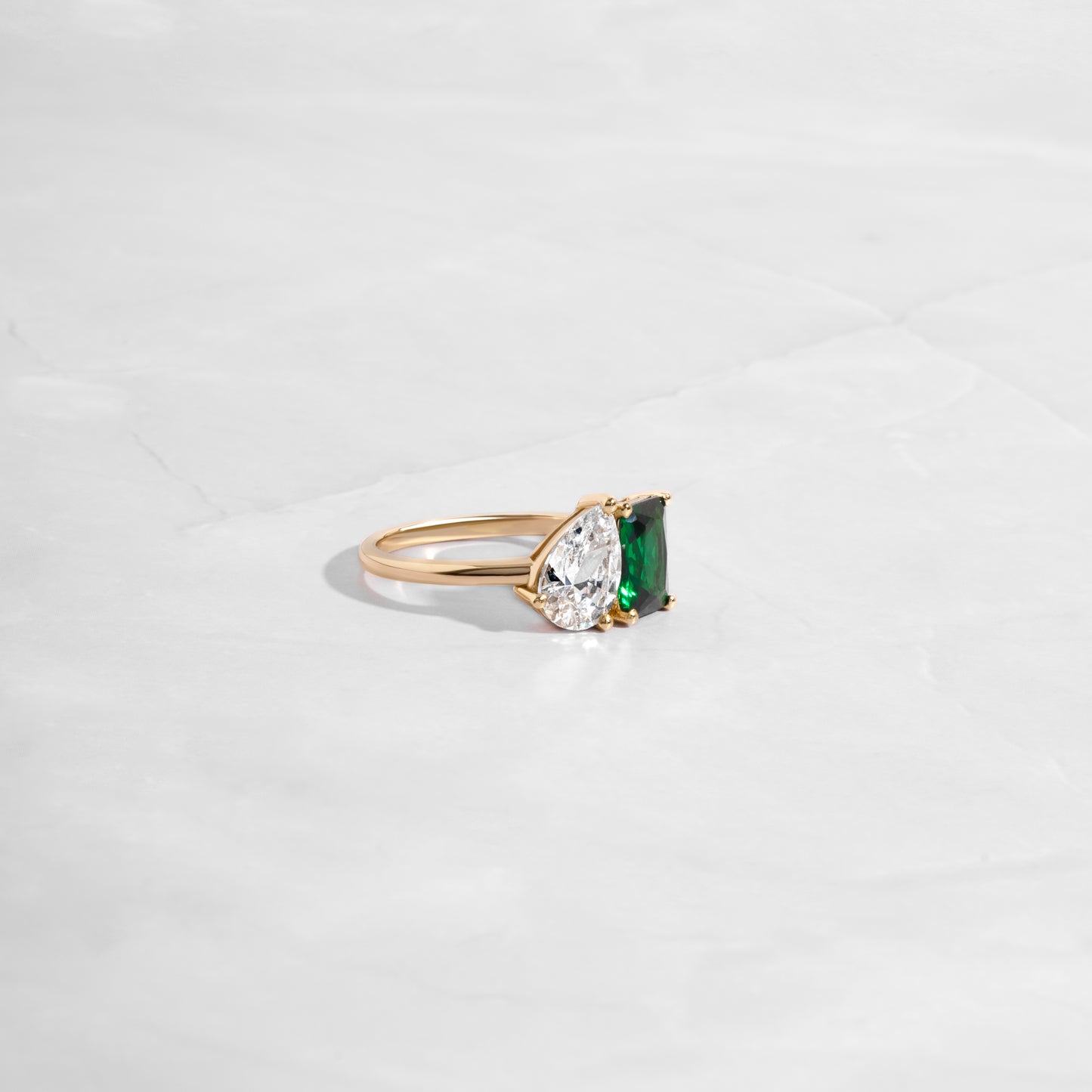 Side profile of Toi et Moi Ring with an emerald cut and pear-shaped diamond, set in gold, as a unique engagement ring or statement ring.