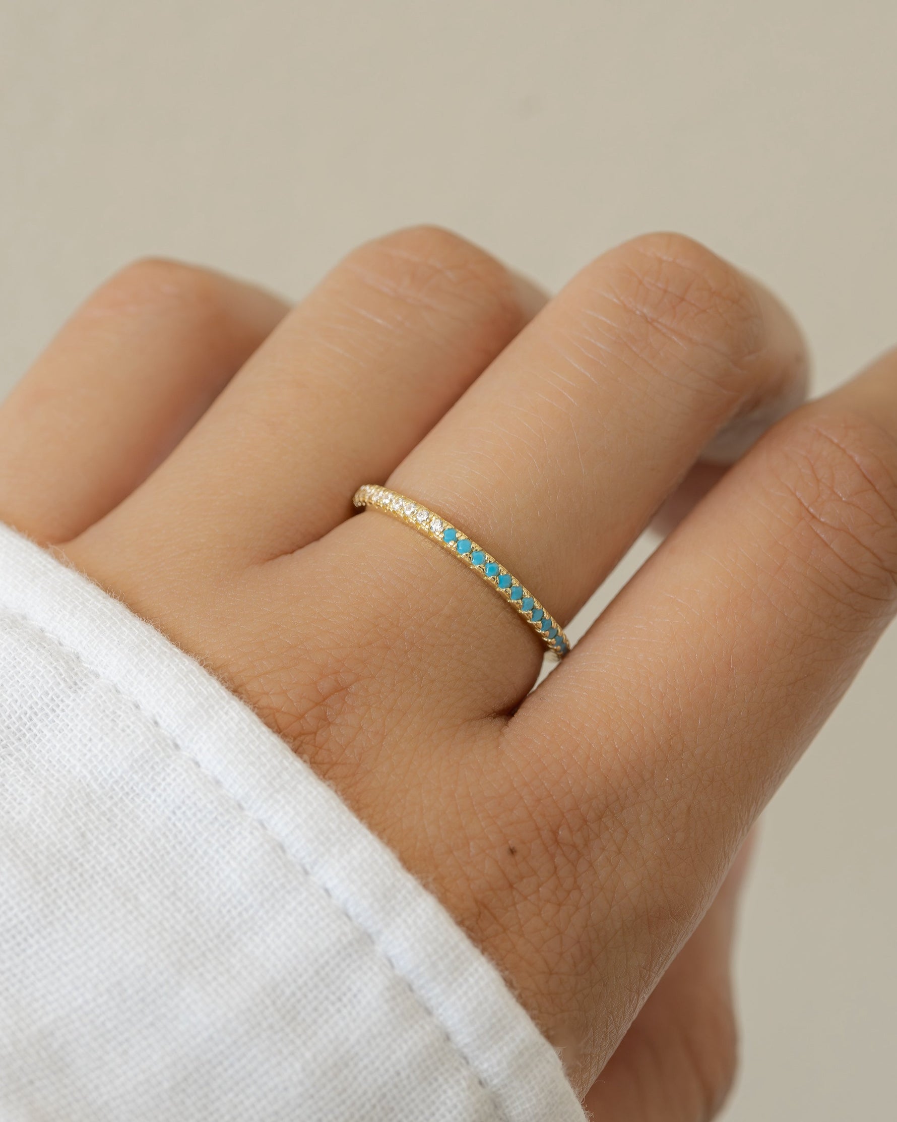 Hand wearing a gold turquoise diamond eternity ring band