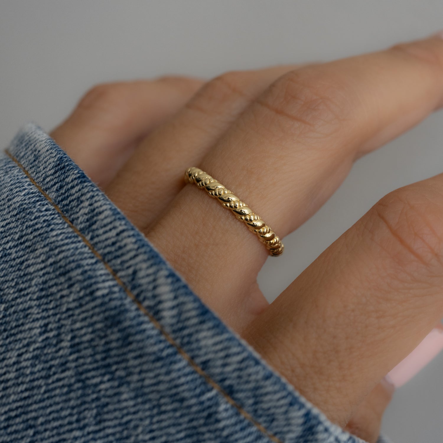 model wearing gold ring with an intricate braided texture, giving a gentle ripple effect. 