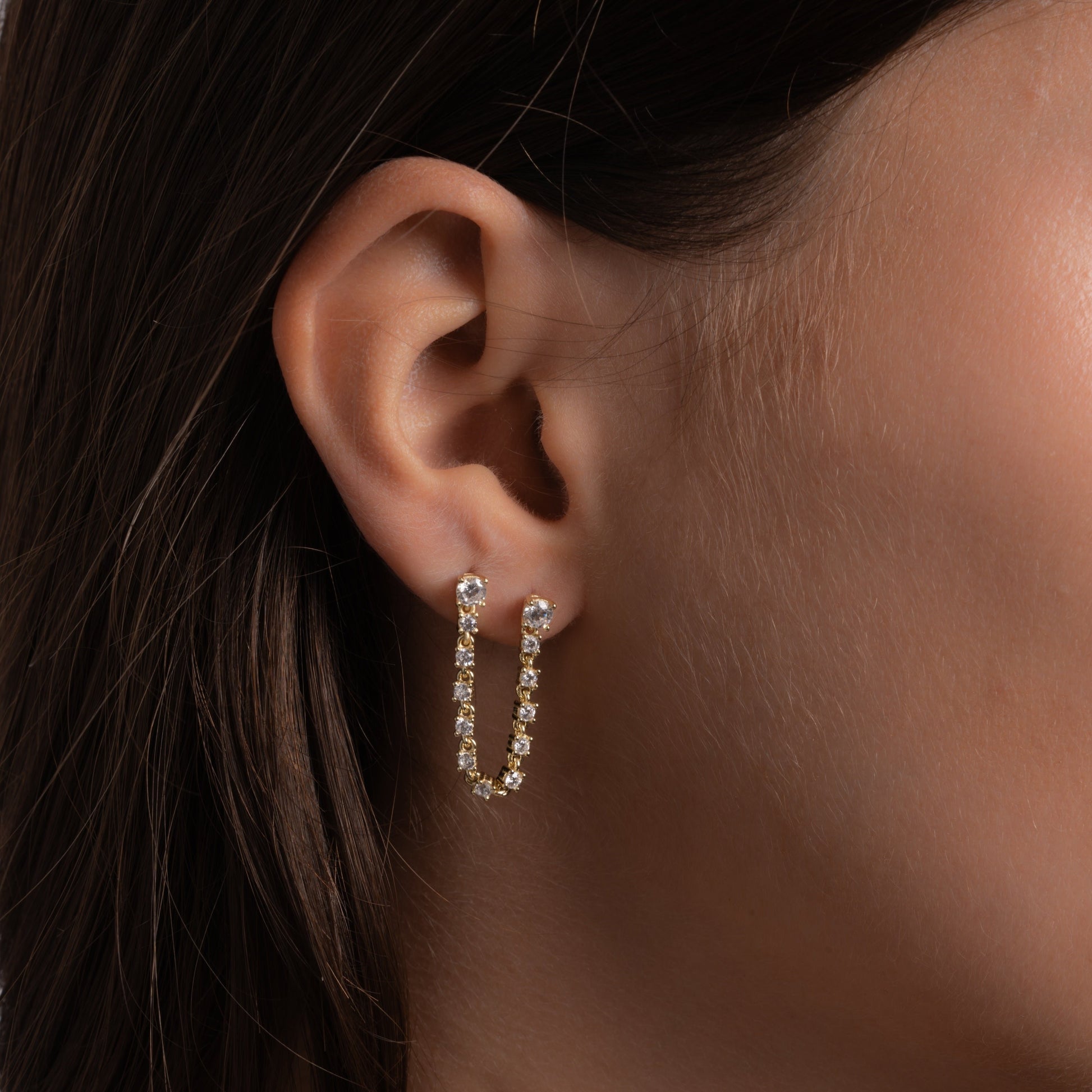 model wearing two-piercing gold dangle earrings linked by a fine tennis chain studded with diamonds.