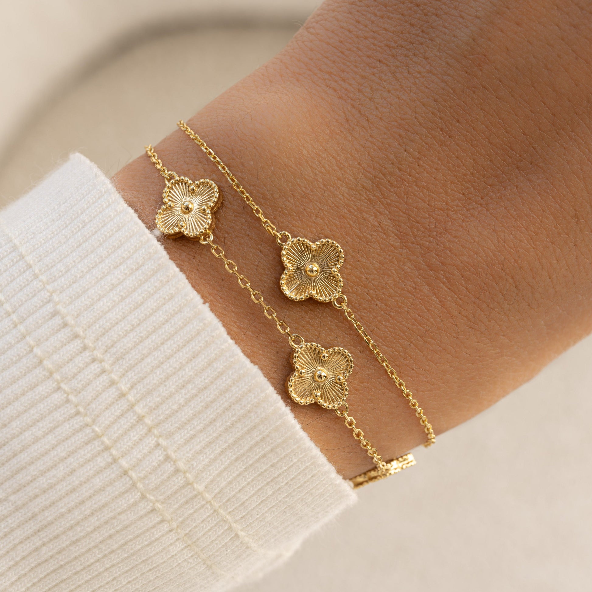 A model wearing two bracelets, one of a four leaf clover bracelet in gold with a charm bracelet with five four clover leaf charms.