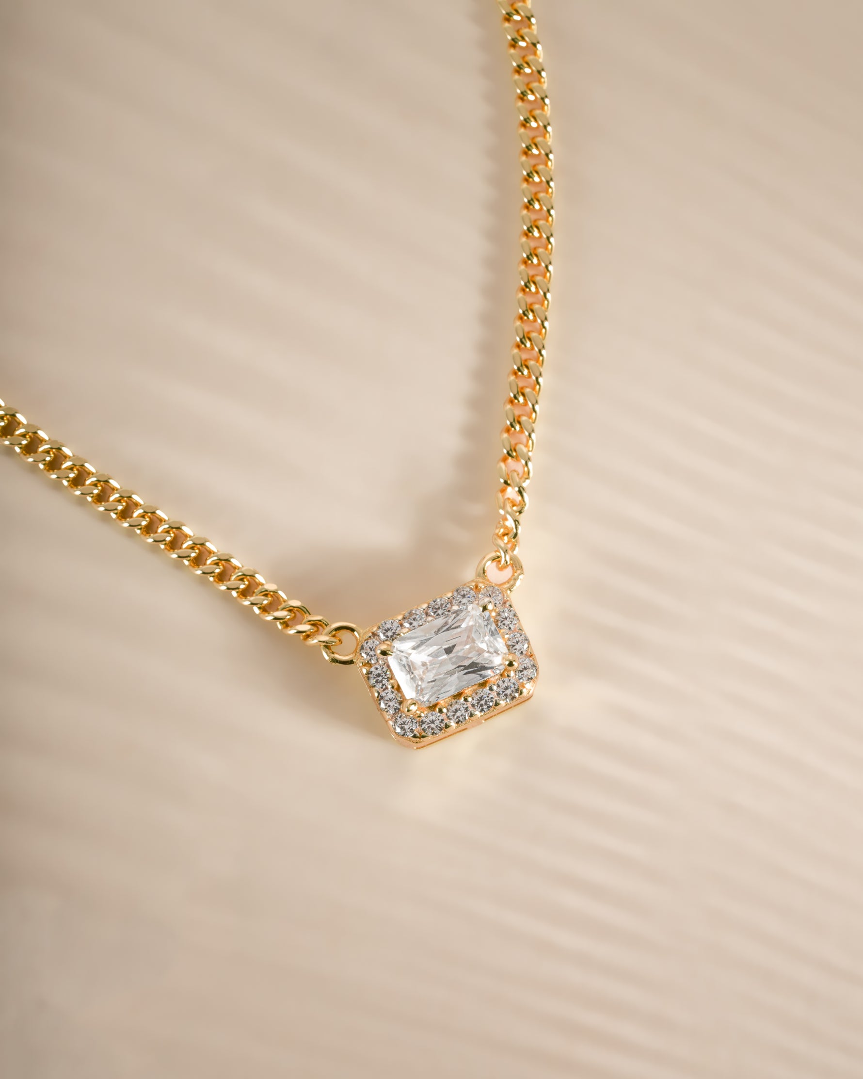 Close-up of Sami Jewels Halo Emerald Cut Necklace on a gold Cuban chain, showcasing the elegant emerald-cut pendant.