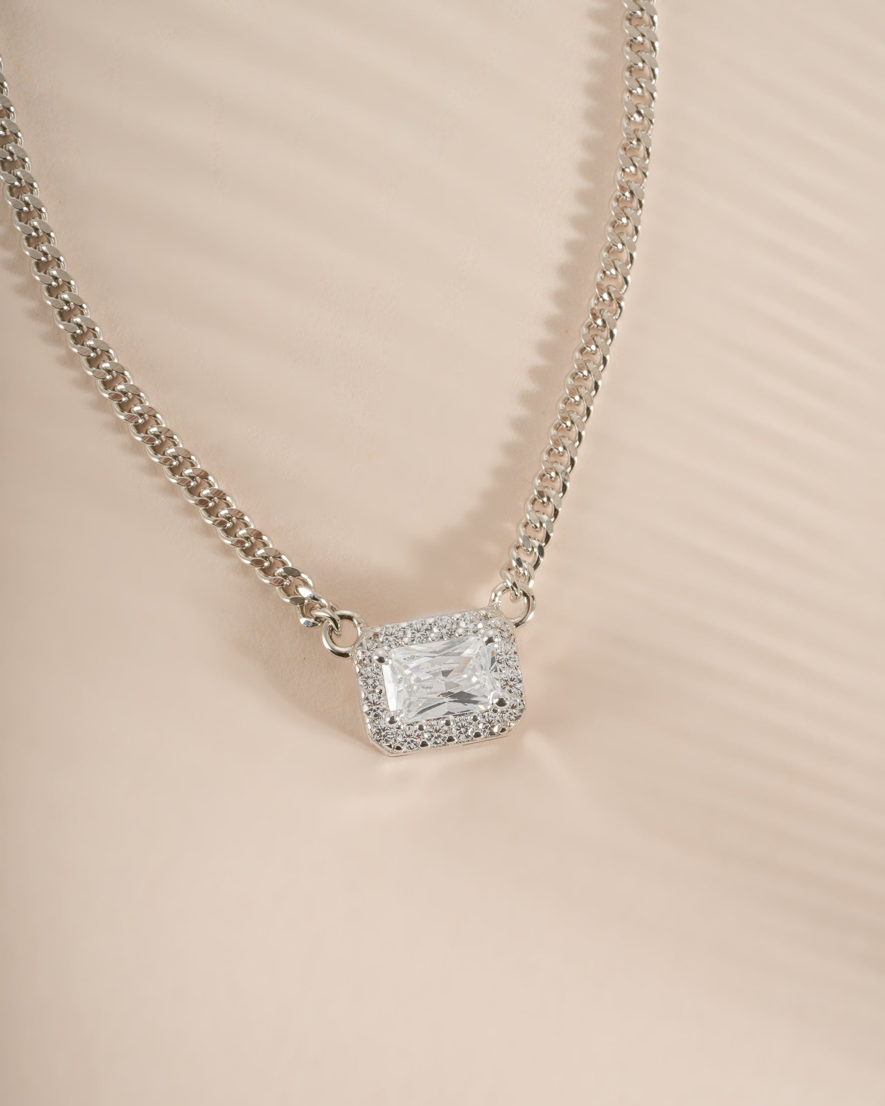 Close-up of Sami Jewels halo emerald cut necklace on a sterling silver Cuban chain, showcasing its elegant design.