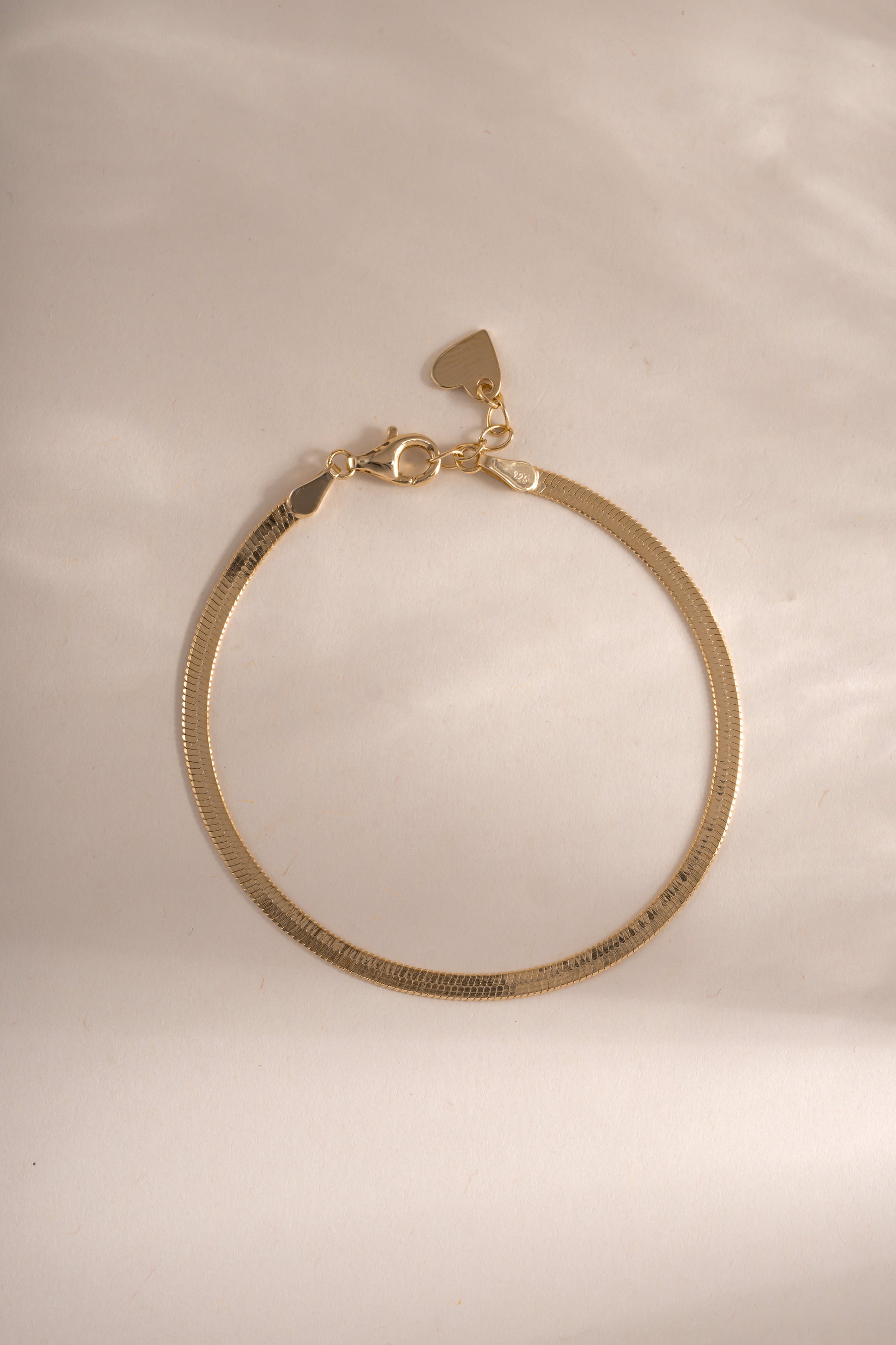 Gold 2mm Herringbone bracelet by Sami Jewels, showcasing its sleek, flat chain design laid out on a neutral background.