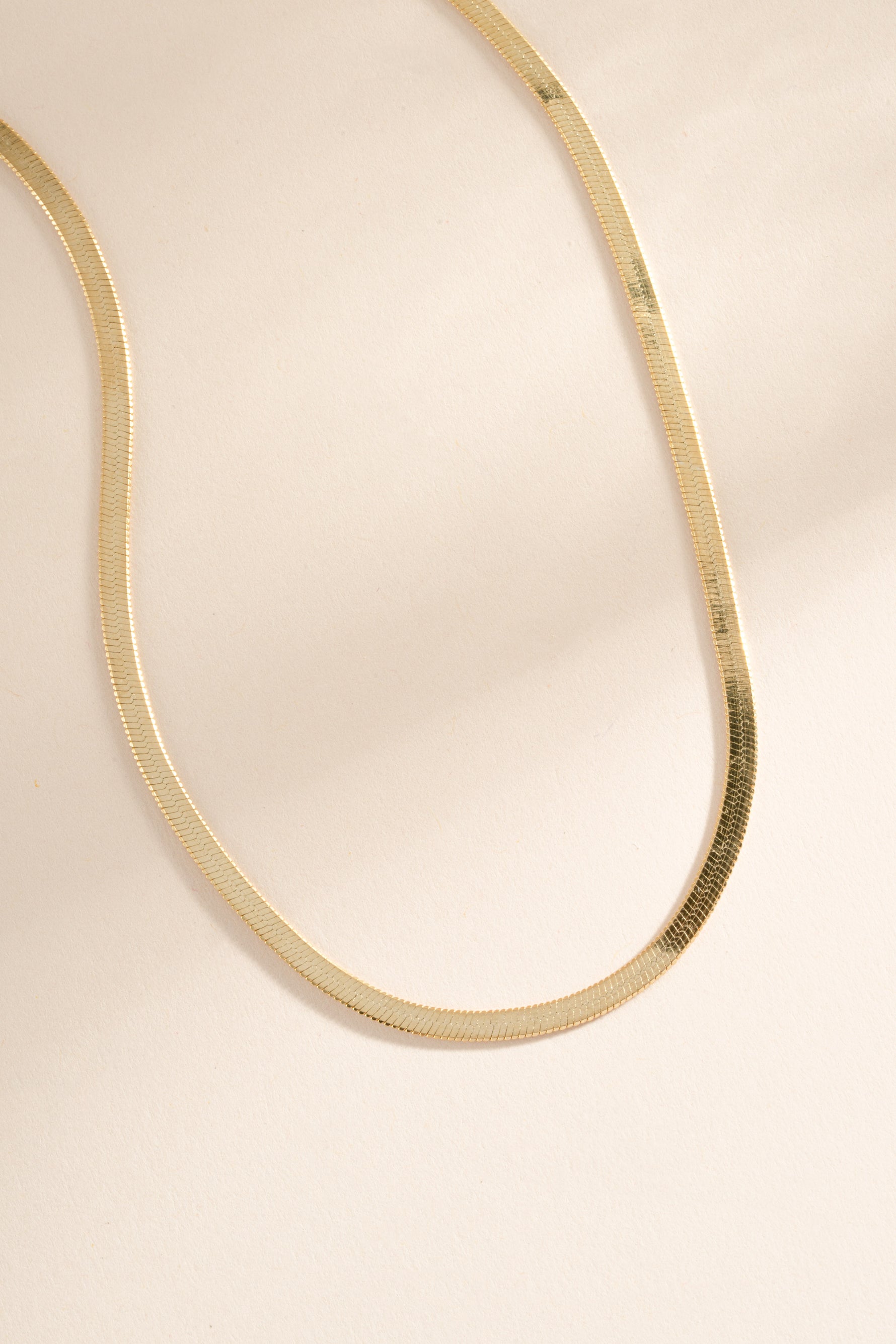 Close-up of a 2mm gold herringbone chain necklace by Sami Jewels showing its smooth, flat woven design.