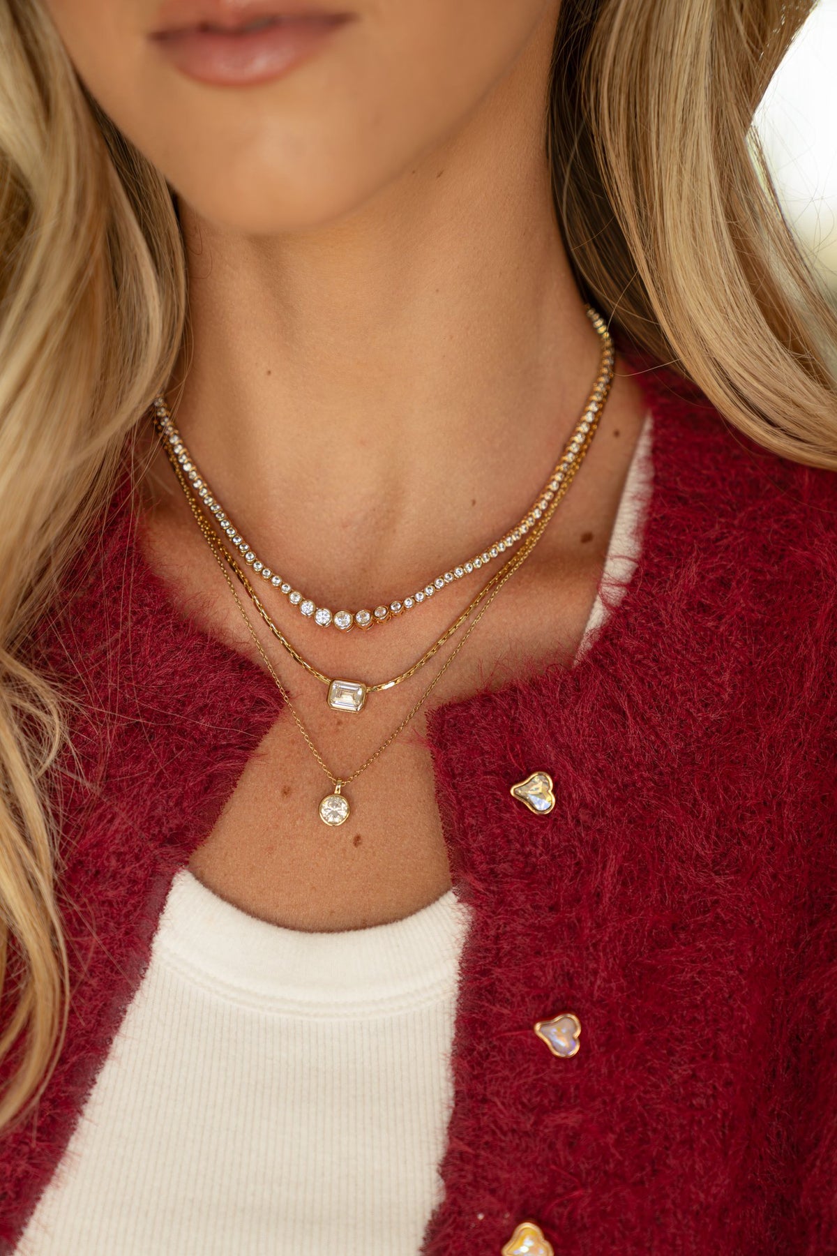 Model wearing layered bezel necklaces with a red knit cardigan