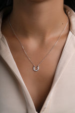 A delicate silver horseshoe pendant necklace worn by a model in a light beige blouse.