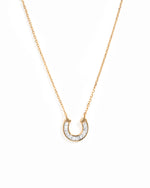 A delicate gold chain necklace featuring a horseshoe-shaped pendant paved with baguette cut stones, set against a plain white background.