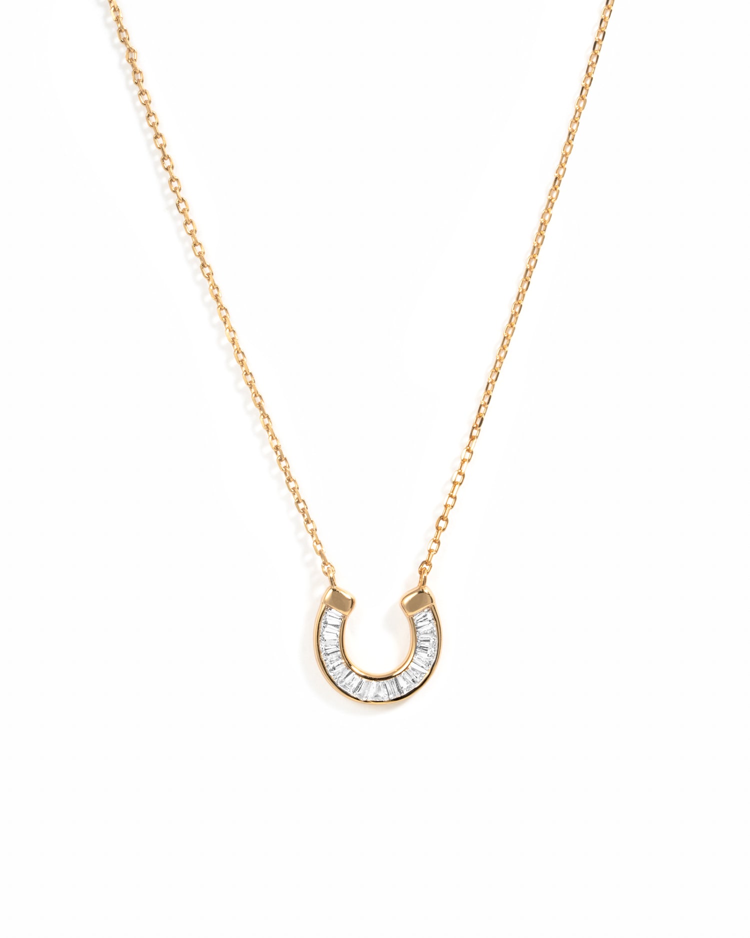 A delicate gold chain necklace featuring a horseshoe-shaped pendant paved with baguette cut stones, set against a plain white background.