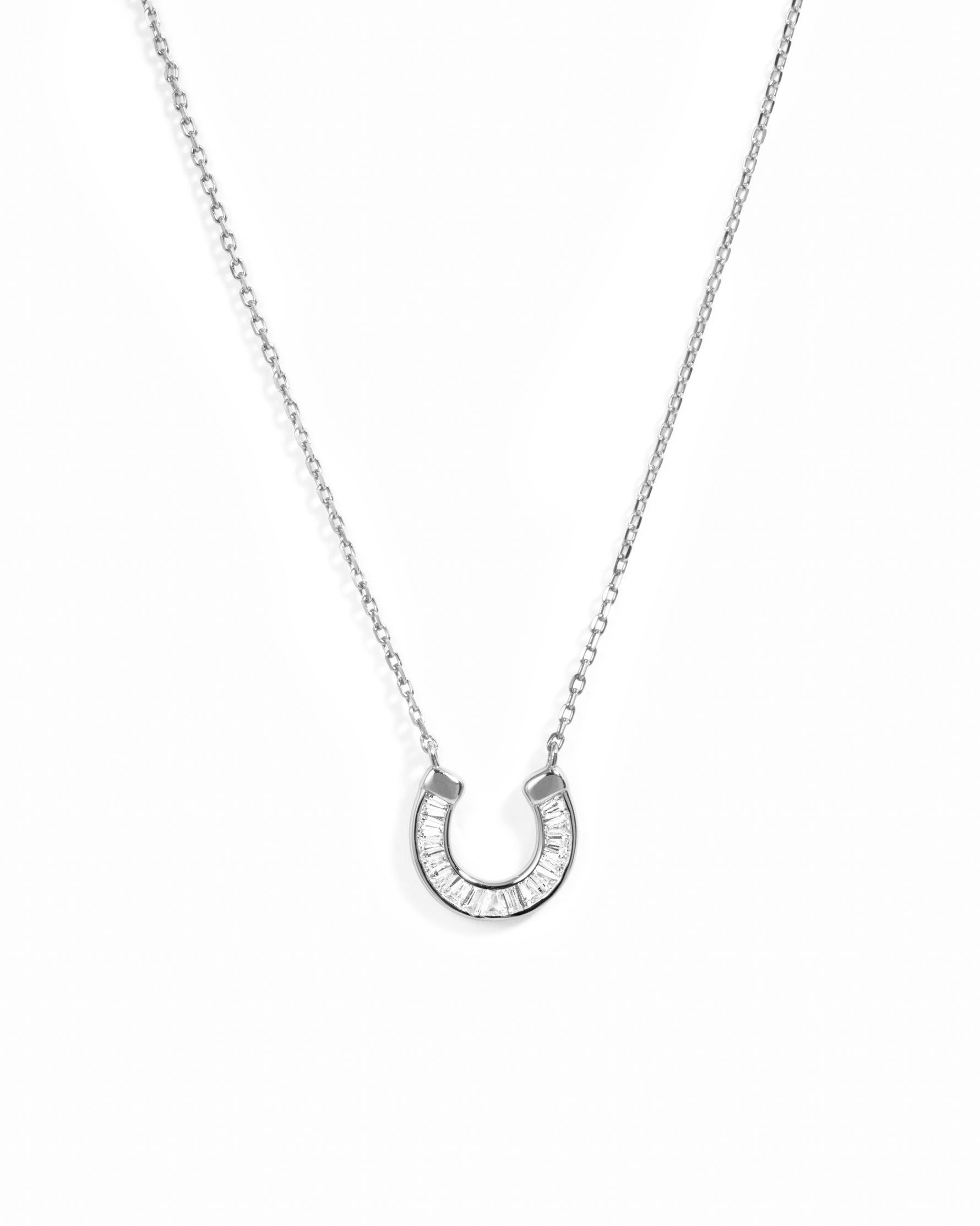 A silver horseshoe pendant necklace set with small clear baguette stones, suspended from a delicate silver chain against a plain white background.
