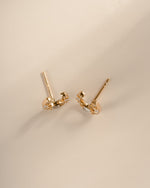 A top view of a pair of gold horseshoe shaped stud earrings embellished with clear baguette and round diamonds, displayed on a neutral beige background.
