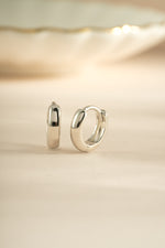 Close-up of minimalist sterling silver huggie hoop earrings by Sami Jewels, showcasing sleek and simple jewelry design.
