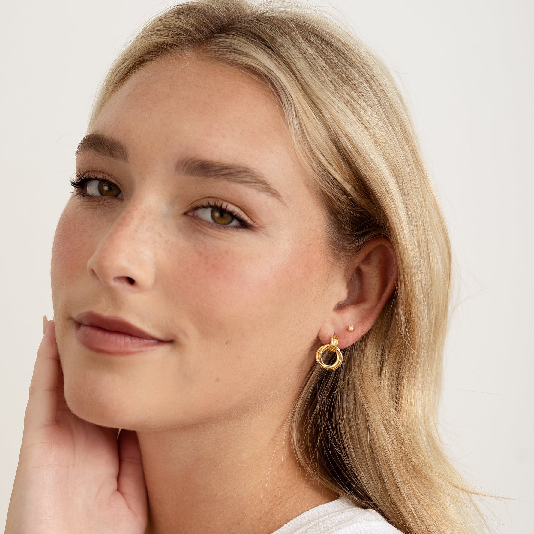 model wearing minimalist gold knot hoops layered with diamond studs for subtle sparkle.