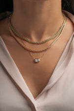 Round emerald tennis necklace stacked with gold chains on model