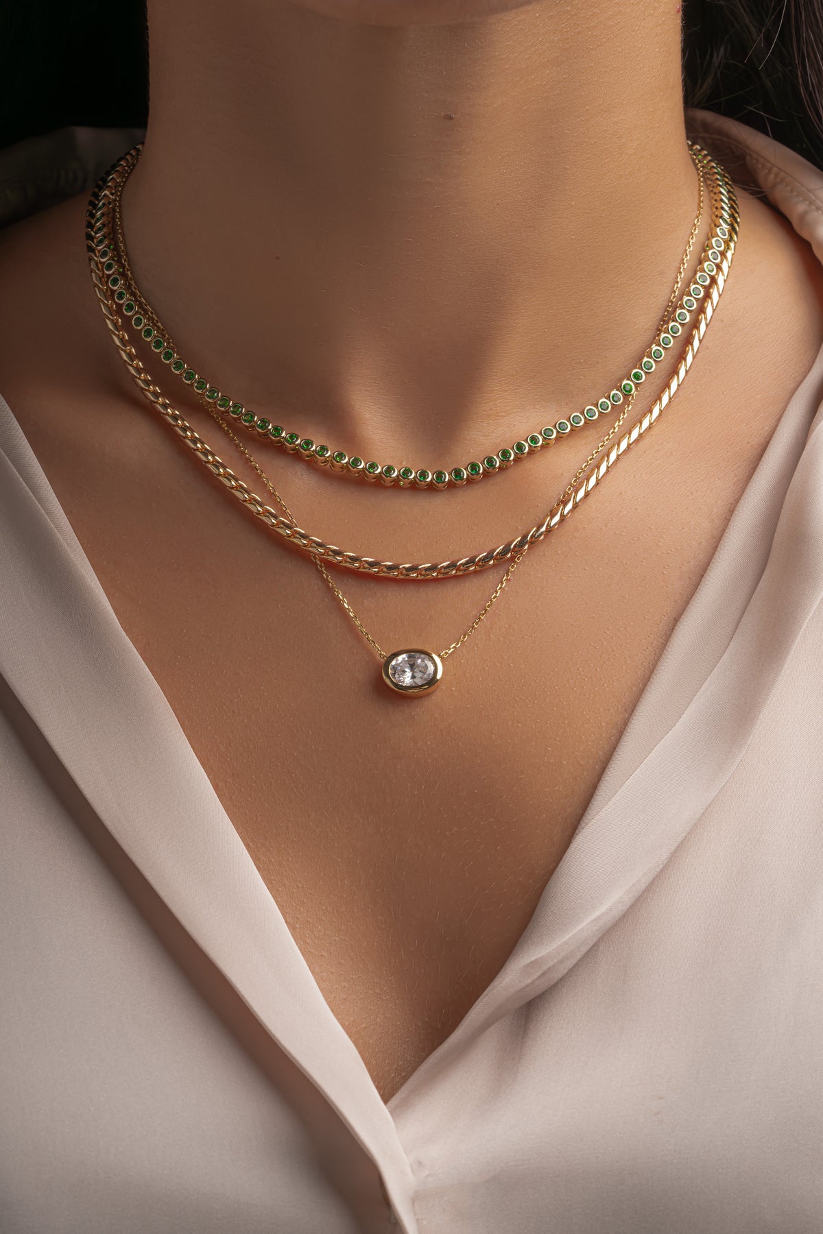 Round emerald tennis necklace stacked with gold chains on model