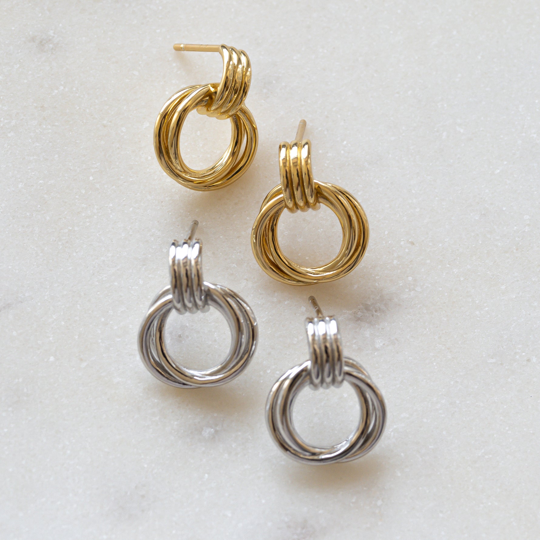 flat lay of gold and silver knot hoop earrings, showcasing delicate yet bold intertwined knot detail.
