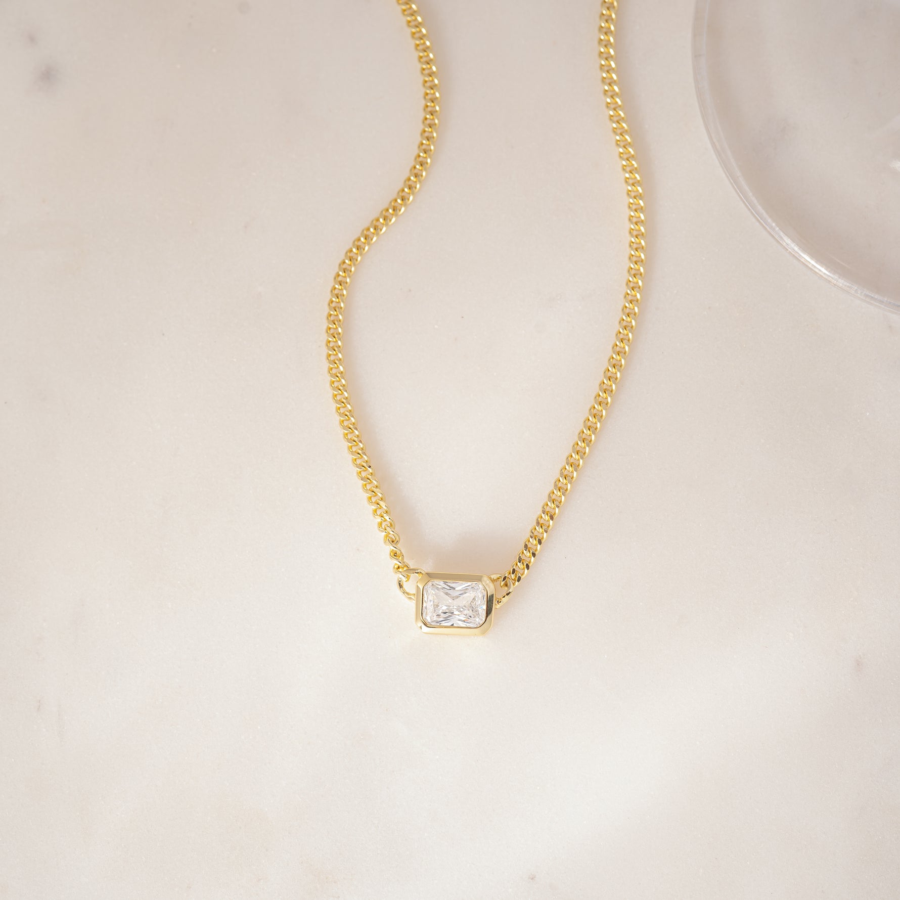 flat lay of an Emerald Cut Pendant in a minimalist bezel setting, hanging on a Cuban chain with a sleek, modern look.