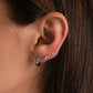 a close up of a model with three piercings, a small silver hoop earring with emerald gemstones in her first piercing, a small sterling silver huggie hoop in her second piercing, and a tiny diamond stud on her third piercing