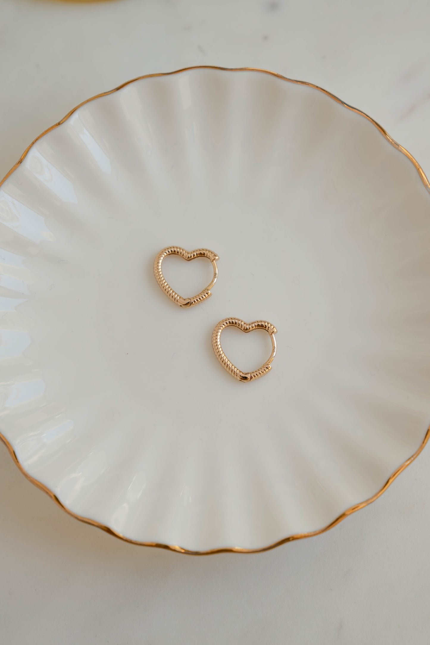 Minimalist gold heart earring hoops for her on white jewelry dish