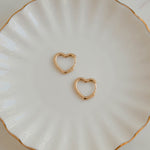 Minimalist gold heart earring hoops for her on white jewelry dish