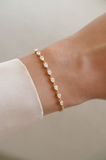 A delicate gold bracelet with small pear cut cz stones, worn on a person's wrist with a white sleeve visible.