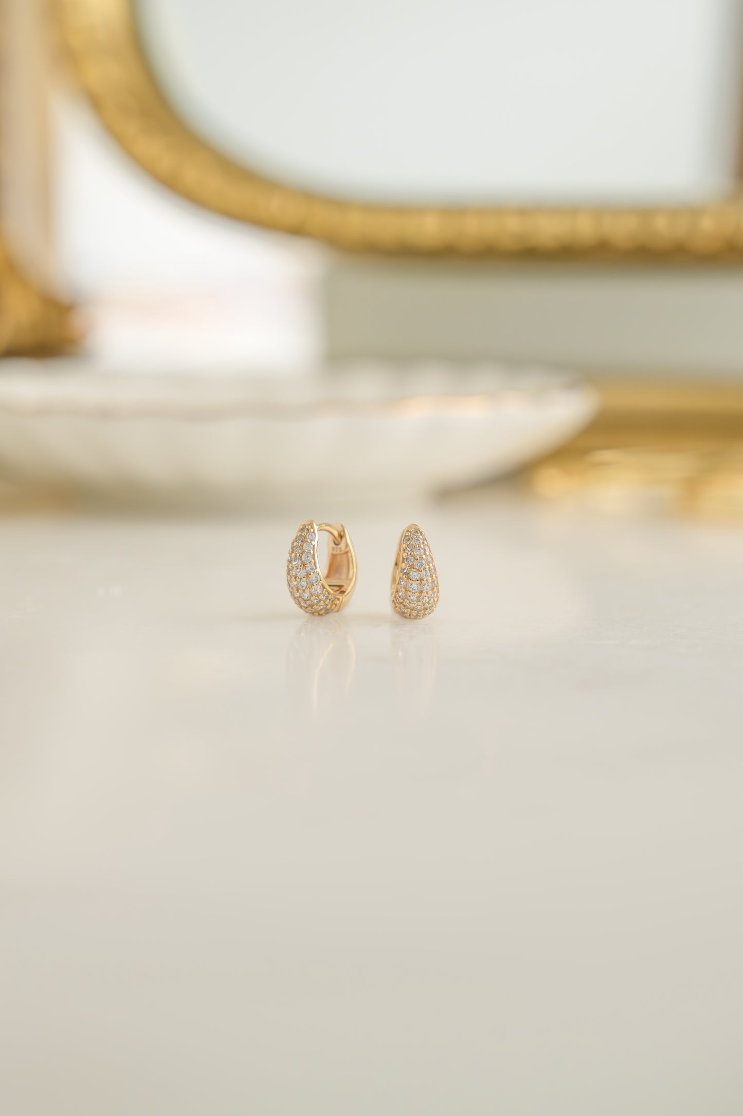 Dainty diamond huggie earrings in 14k gold plated finish on white marble