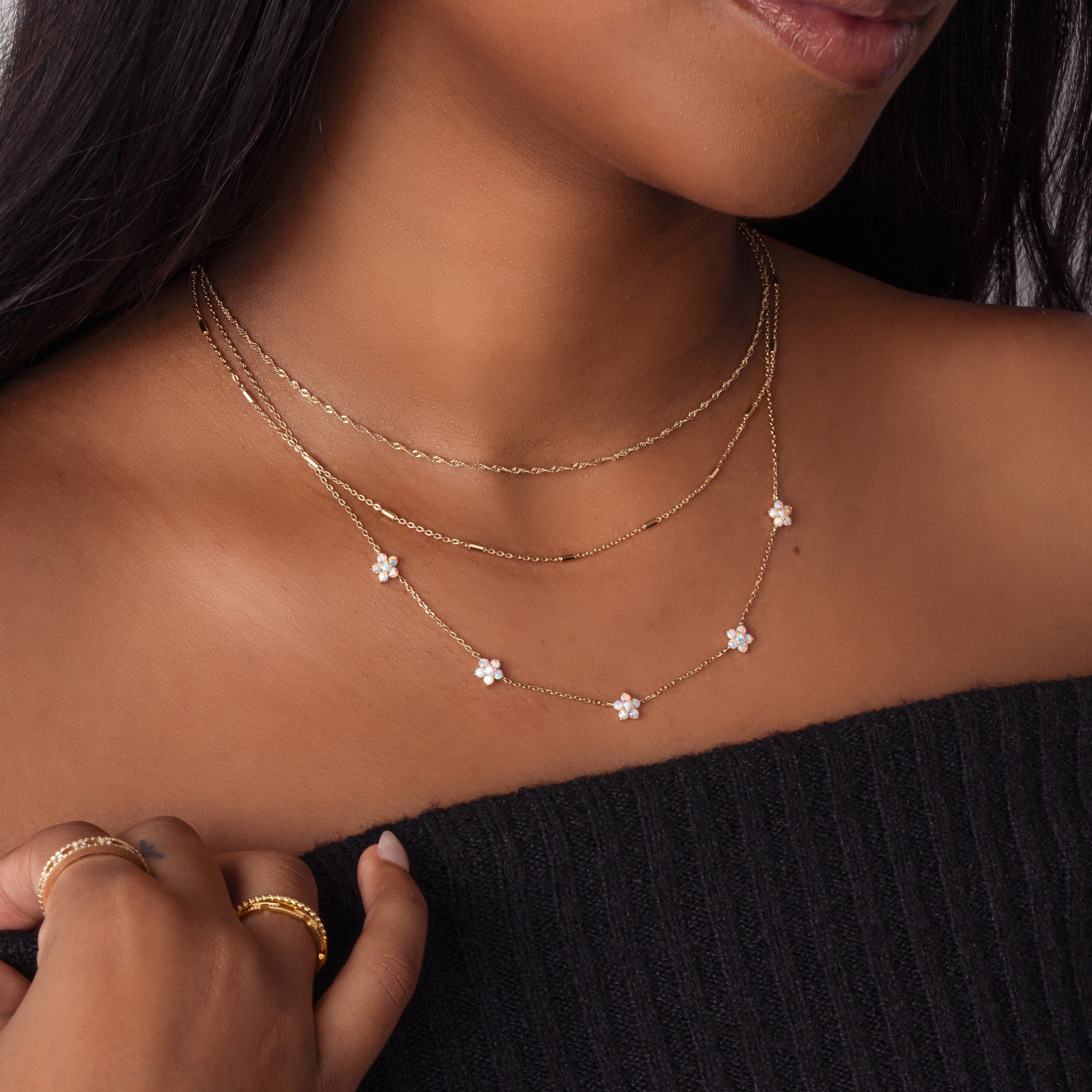 Model wearing layered gold necklaces, dainty gold chain necklaces with minimalist opal charm necklace.