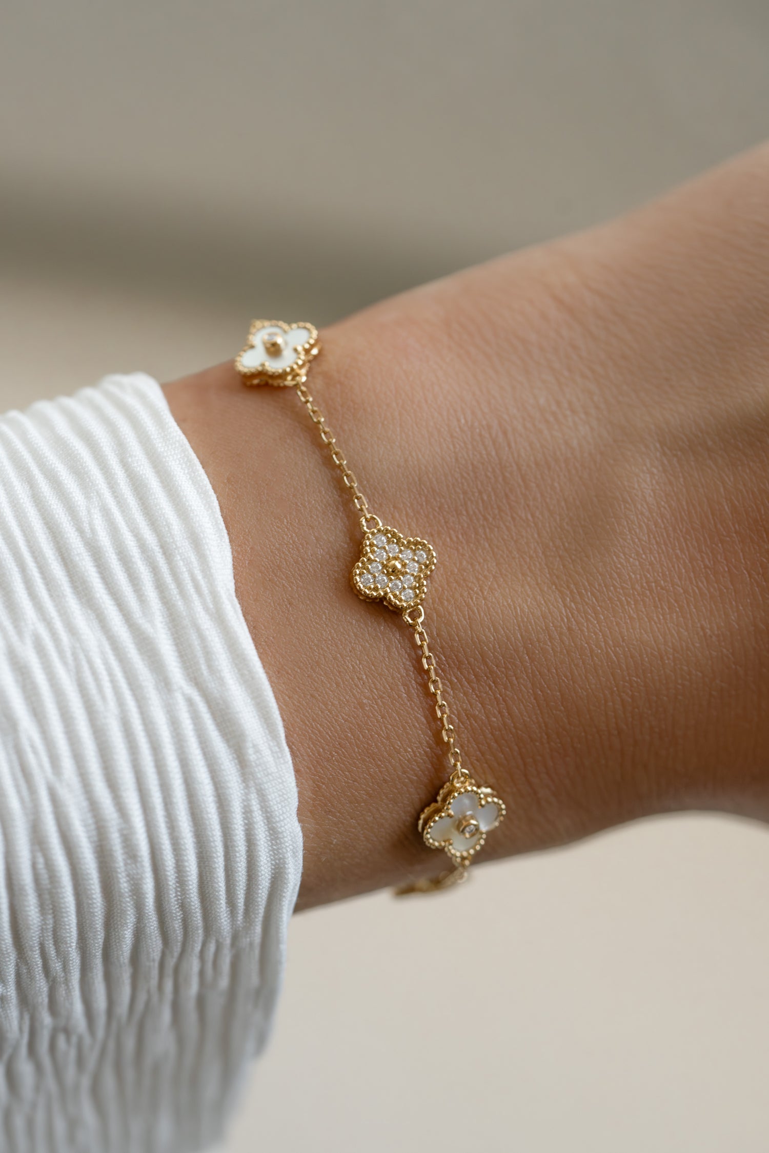 Gold bracelet with a mother-of-pearl four-leaf clover charm, stylish jewelry by Sami Jewels on a woman's wrist.