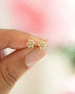 opal flower studs in gold held between two fingers