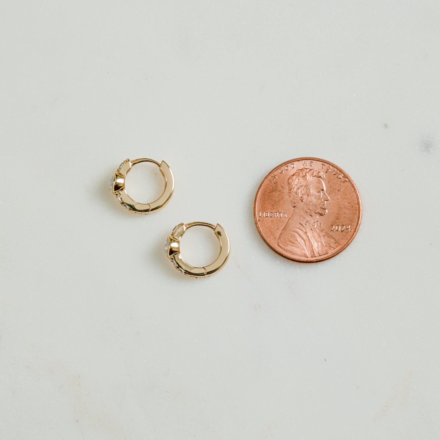 Close up image of sterling silver studded cz opal earrings. The baby gold hoop huggie earrings are being compared to a penny for size reference. 