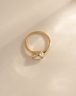 A side profile of a  gold ring with a bezel-set cz stone, photographed on a warm beige background with soft shadows.
